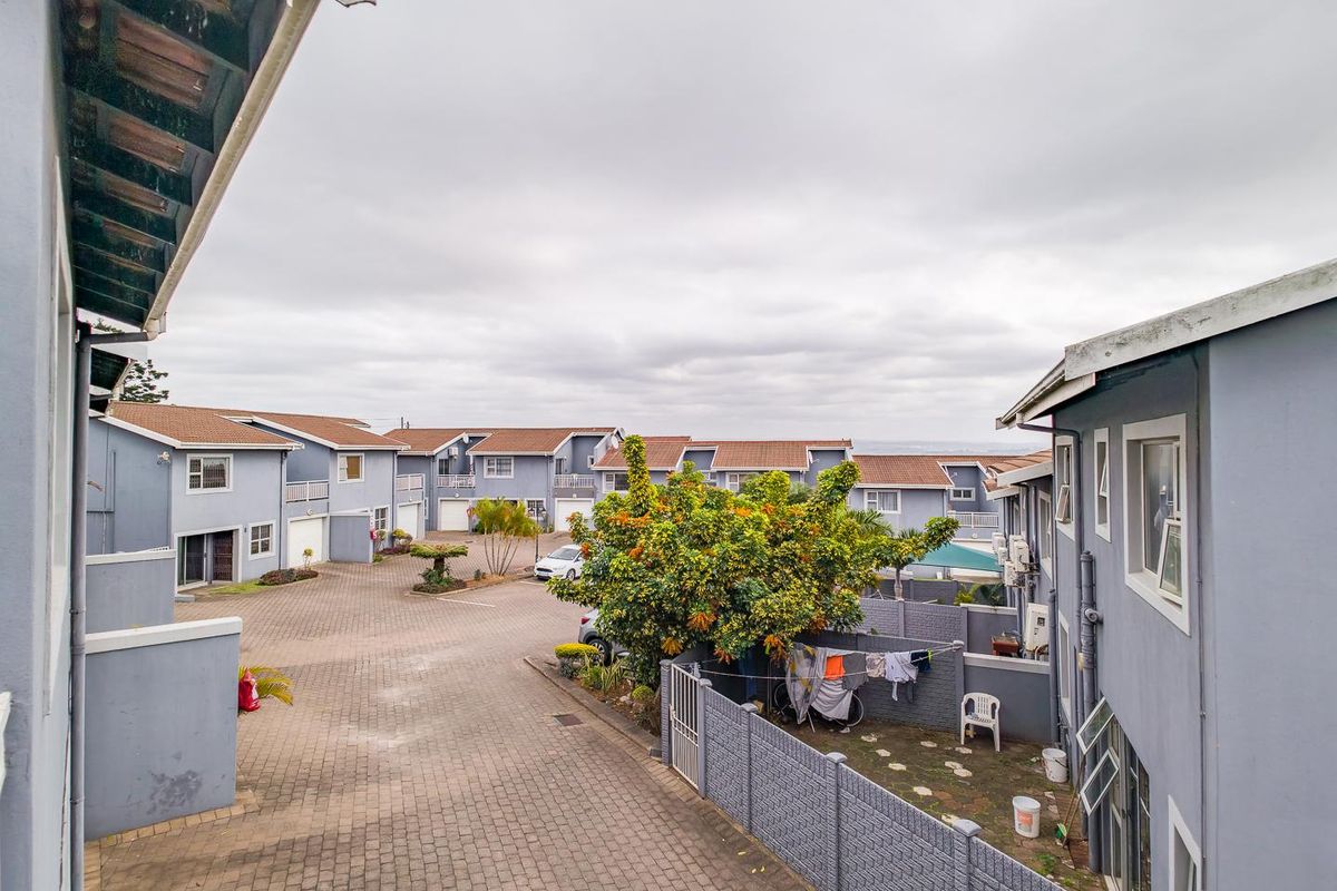 An elevated view of a residential apartment complex courtyard featuring paved driveways, boundary walls, and multiple unit facades with tiled roofing.