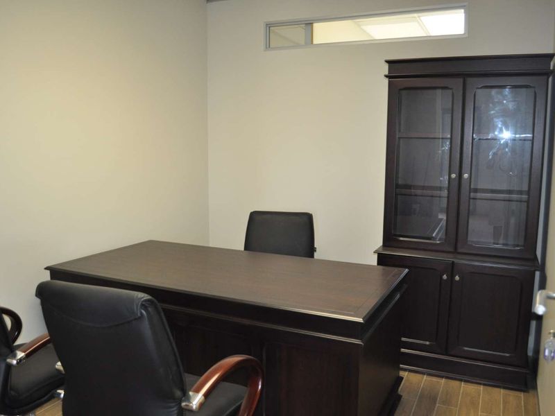 A professional office space featuring neutral walls, wood-look flooring, and a high-level transom window for natural light.