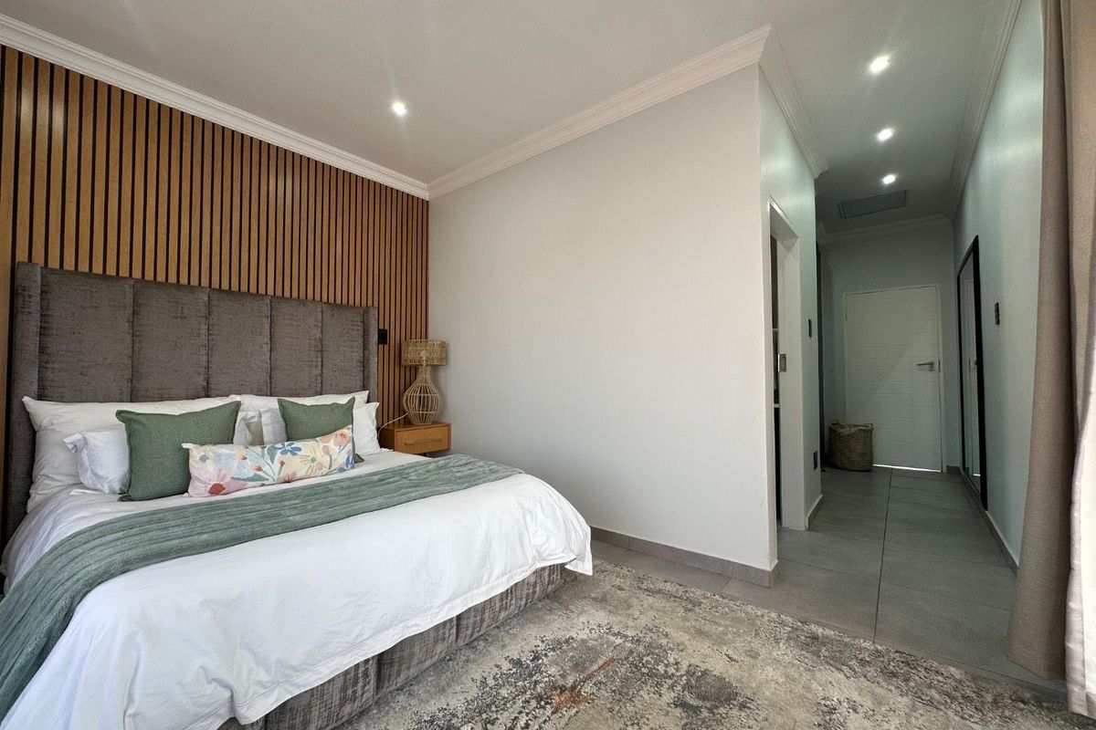 A modern bedroom featuring a decorative timber slat feature wall, recessed downlighting, and tiled flooring leading into a hallway.
