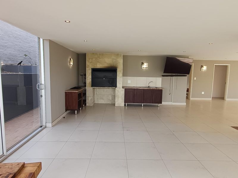 Spacious open-plan living area featuring a built-in braai, kitchenette with sink, and large sliding glass doors leading to an outdoor patio.