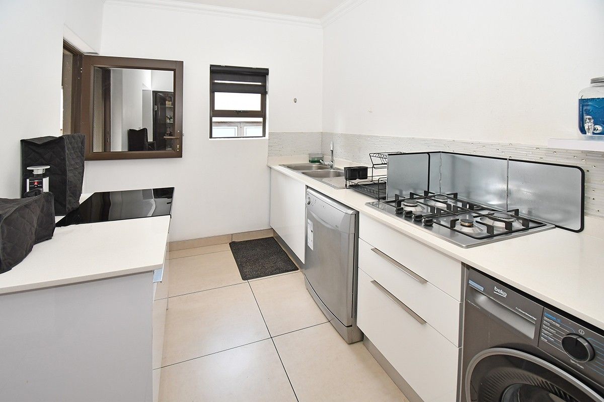 A functional kitchen featuring white cabinetry, a gas hob, tiled backsplash, and tiled flooring, providing a clean and practical workspace.