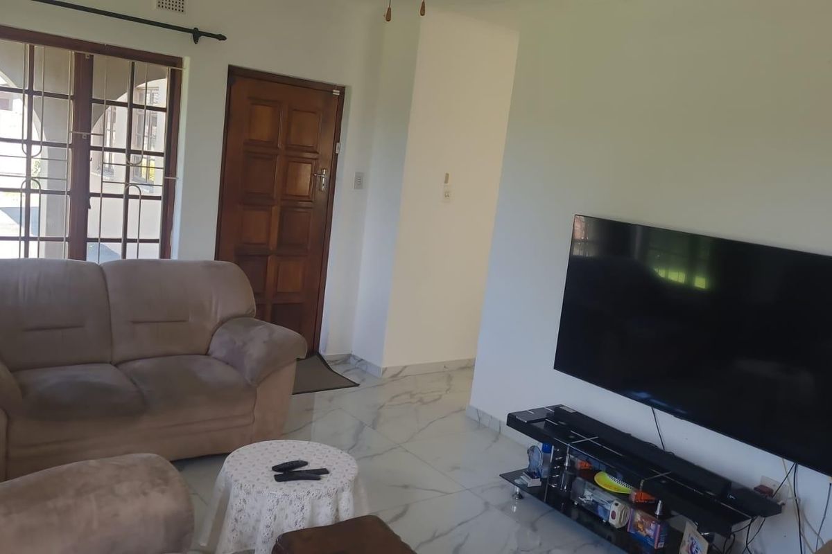 A living room featuring marble-look floor tiles, a wooden entrance door, and a security gate over the window.