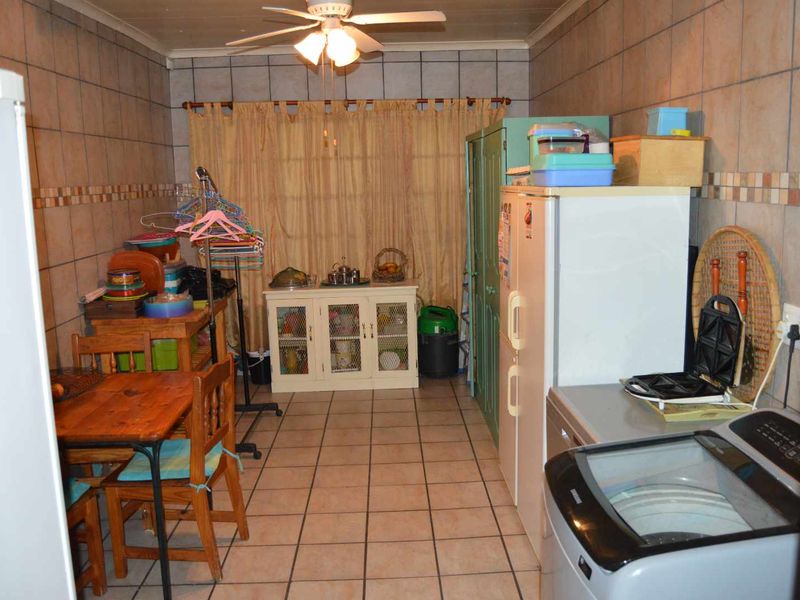 A functional laundry area featuring tiled walls and floors, equipped with a ceiling fan and ample space for utility appliances.