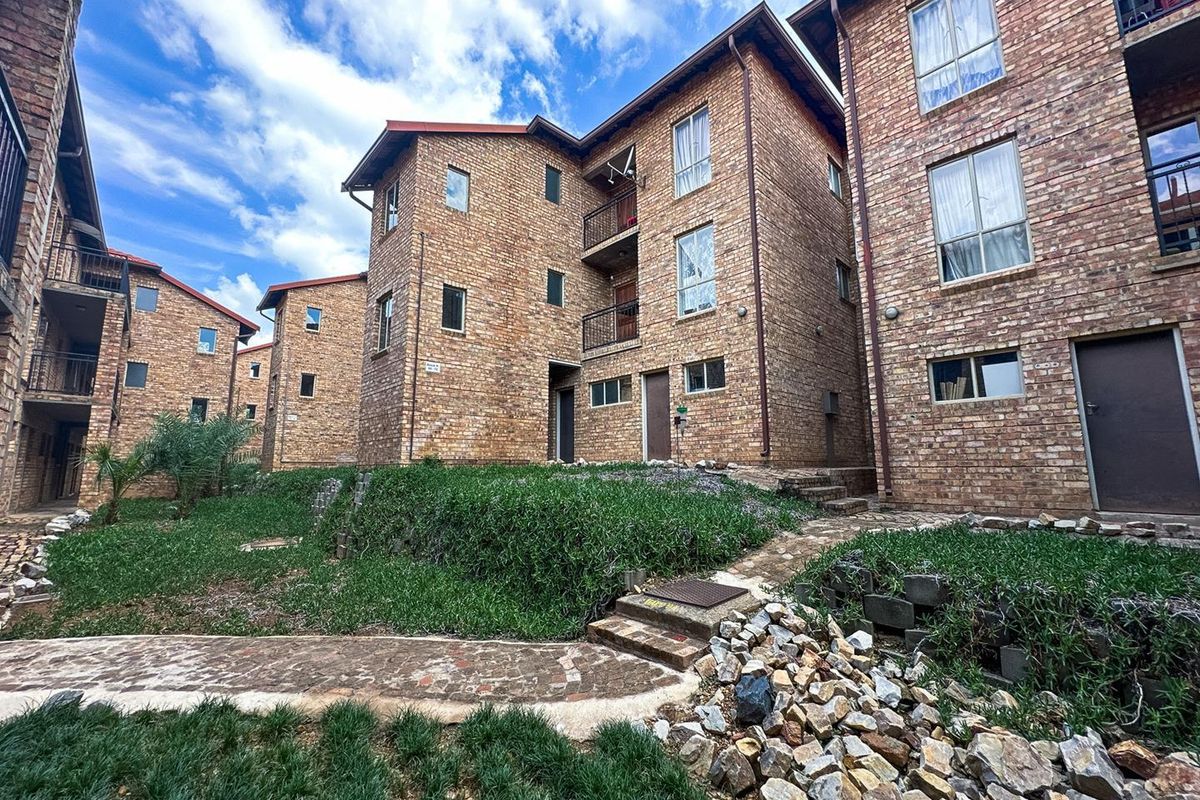 Exterior view of a multi-story apartment complex featuring face brick construction, private balconies, and established garden landscaping with paved pathways.