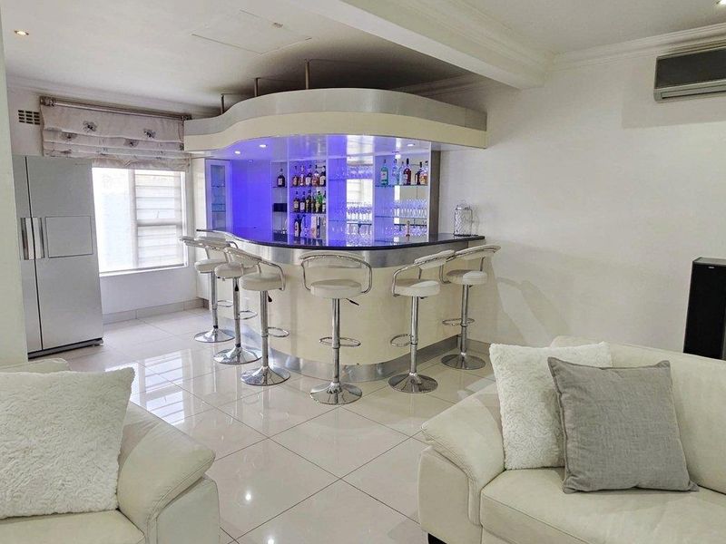 A modern, well-lit home bar area featuring a curved built-in counter, integrated shelving, and polished tile flooring, creating a sophisticated entertainment space.
