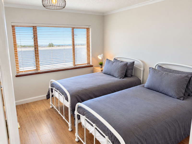 A bright and well-maintained bedroom featuring laminate flooring, neutral walls, and a large window with fitted blinds.