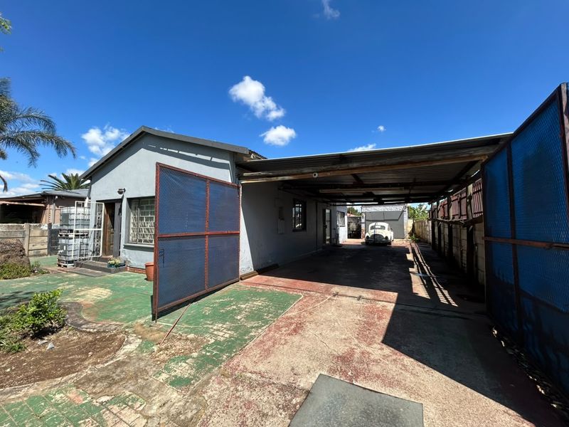 Front exterior view of the property featuring a large carport, paved driveway, and secure metal gate entrance.