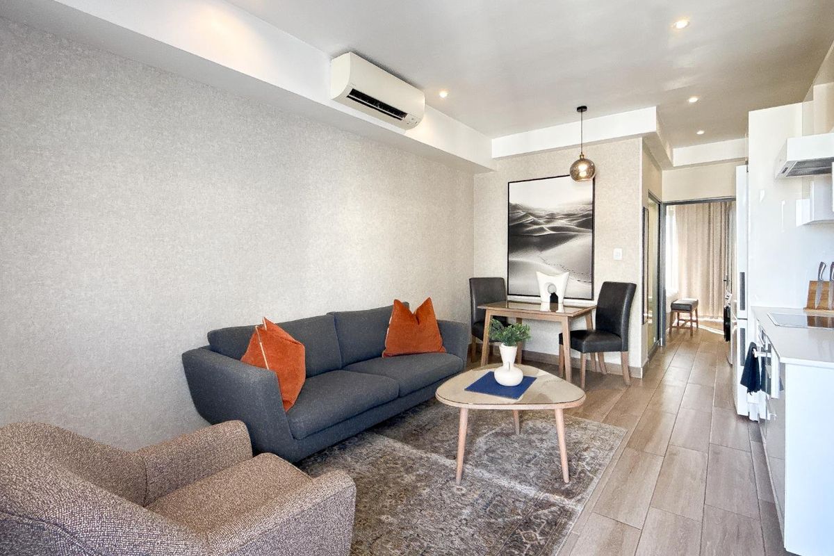 Modern open-plan living area featuring tiled flooring, recessed lighting, and a wall-mounted air conditioning unit, seamlessly integrated with a functional kitchen space.