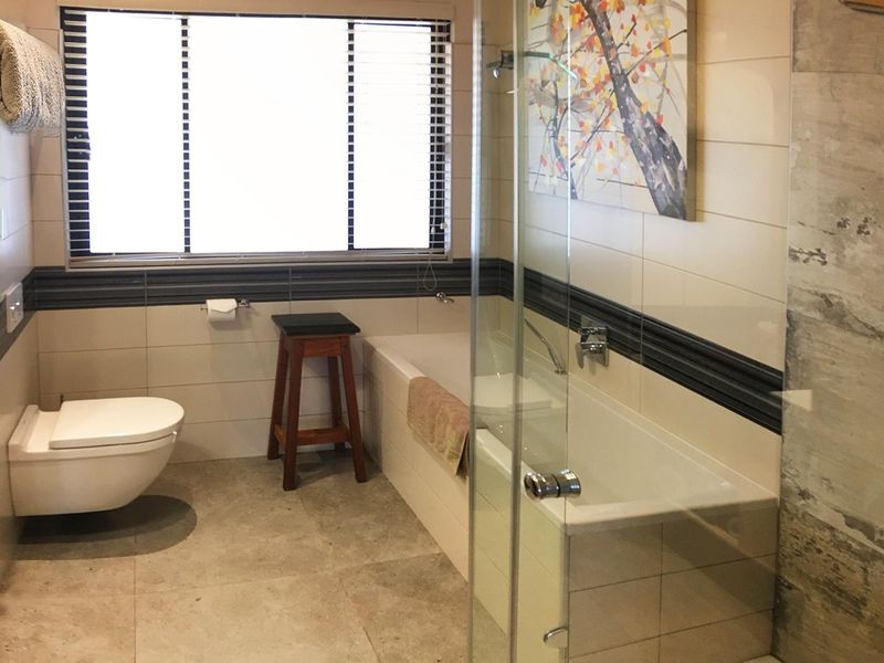 Modern bathroom featuring a wall-mounted toilet, built-in bathtub, and a separate glass-enclosed shower with neutral tiled finishes.