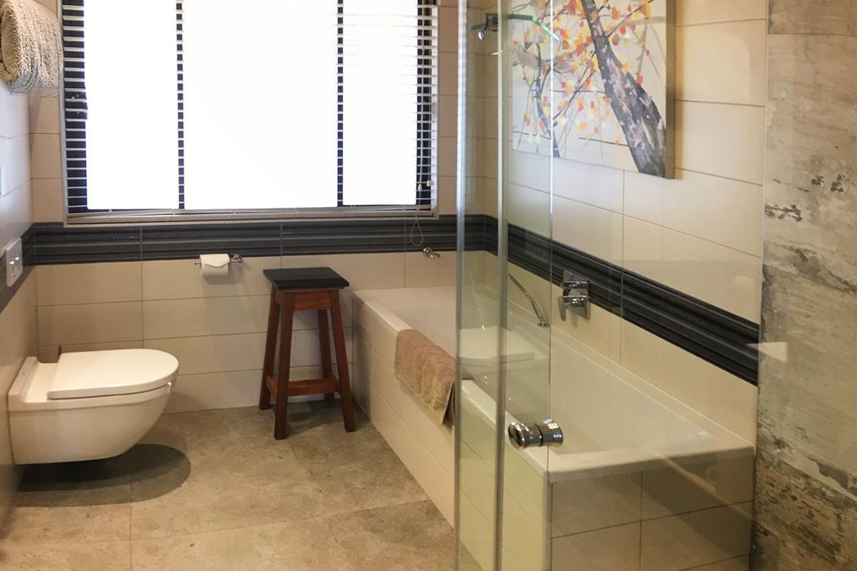 Modern bathroom featuring a wall-mounted toilet, built-in bathtub, and a separate glass-enclosed shower with neutral tiled finishes.