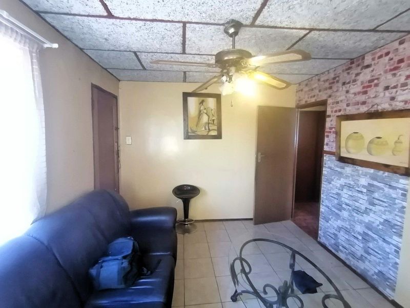 Living room featuring tiled flooring, a ceiling fan, and decorative brick-effect wall cladding.