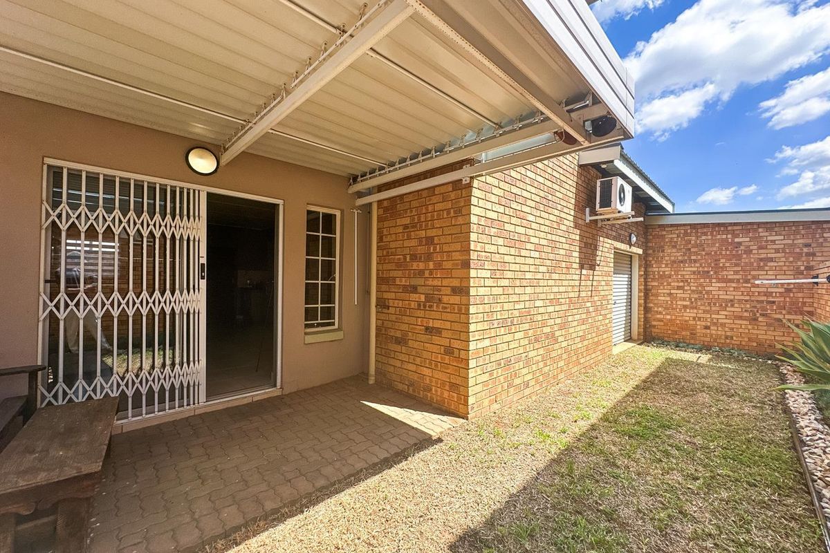 A rear exterior view featuring a covered patio area with brick walls, security gate, and a small adjacent garden space.