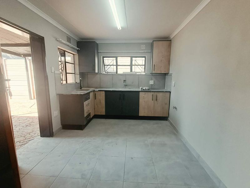 A functional, empty kitchen featuring modern two-tone cabinetry, tiled backsplash, and tiled flooring, ready for appliance installation.