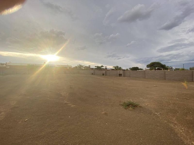 A vacant residential plot featuring a perimeter masonry wall and built-in braai area, captured during sunset.