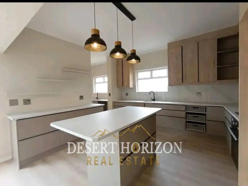 Modern kitchen featuring a central island, quartz countertops, sleek cabinetry, integrated appliances, and contemporary pendant lighting in a bright, open-plan layout.