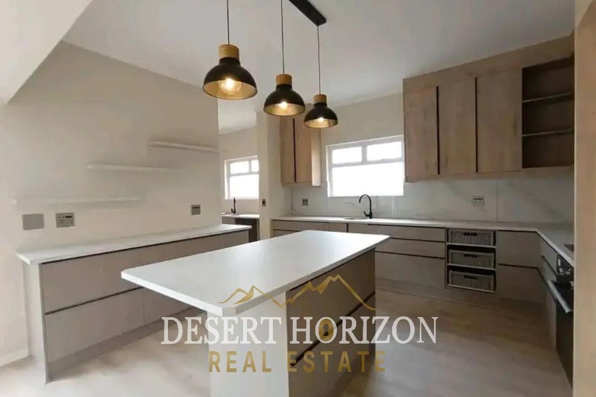 Modern kitchen featuring a central island, quartz countertops, sleek cabinetry, integrated appliances, and contemporary pendant lighting in a bright, open-plan layout.