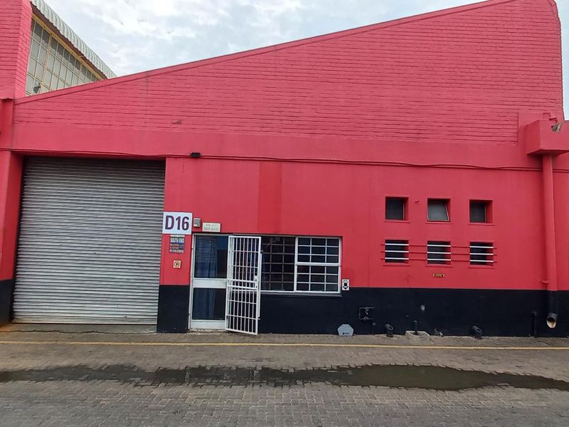 Industrial unit exterior featuring a prominent red brick facade, roller shutter door, and secure pedestrian entrance with security gate.