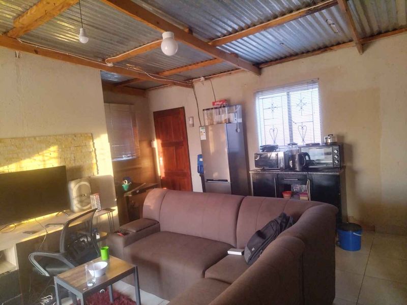 Open plan living area featuring exposed corrugated metal roofing, timber rafters, tiled flooring, and security bars on windows.