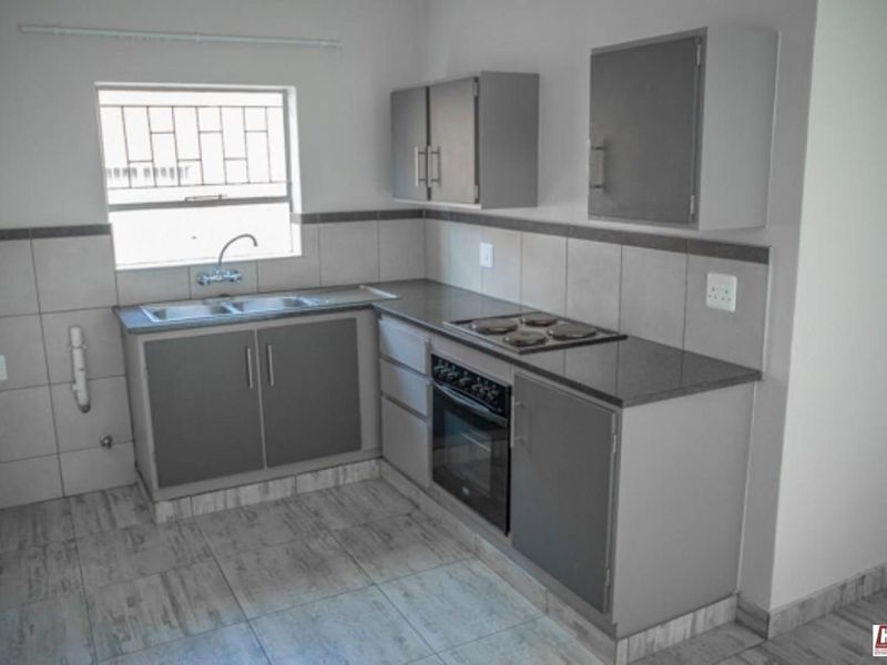 A clean, functional kitchen featuring grey built-in cabinetry, a stainless steel sink, electric hob, built-in oven, and neutral tiled finishes.