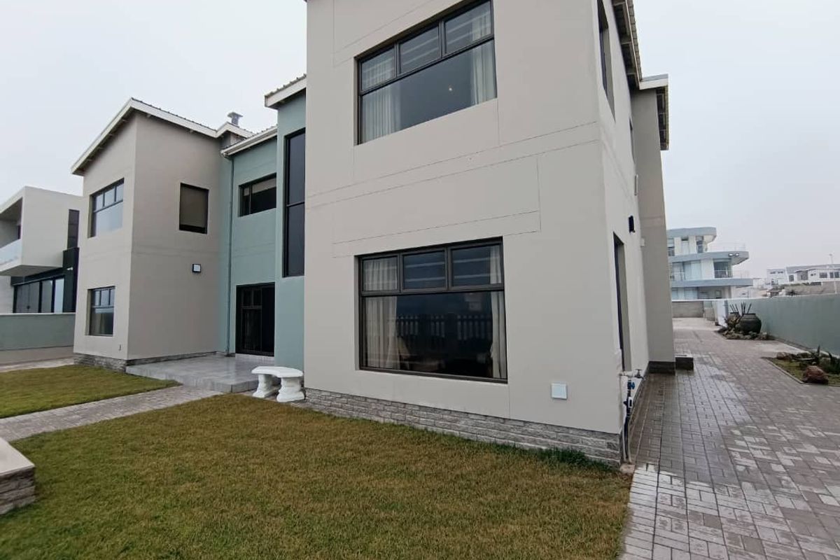 A modern two-story residential exterior featuring clean lines, stone cladding accents, large aluminium-framed windows, and a paved walkway leading to a tiled patio area.