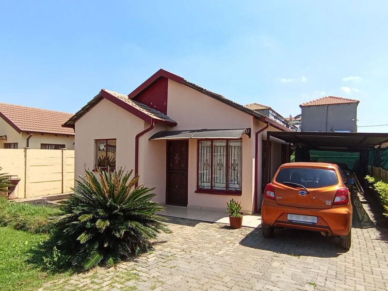 Front view of a single-story residential house featuring a paved driveway, attached carport, and security features on windows and doors.