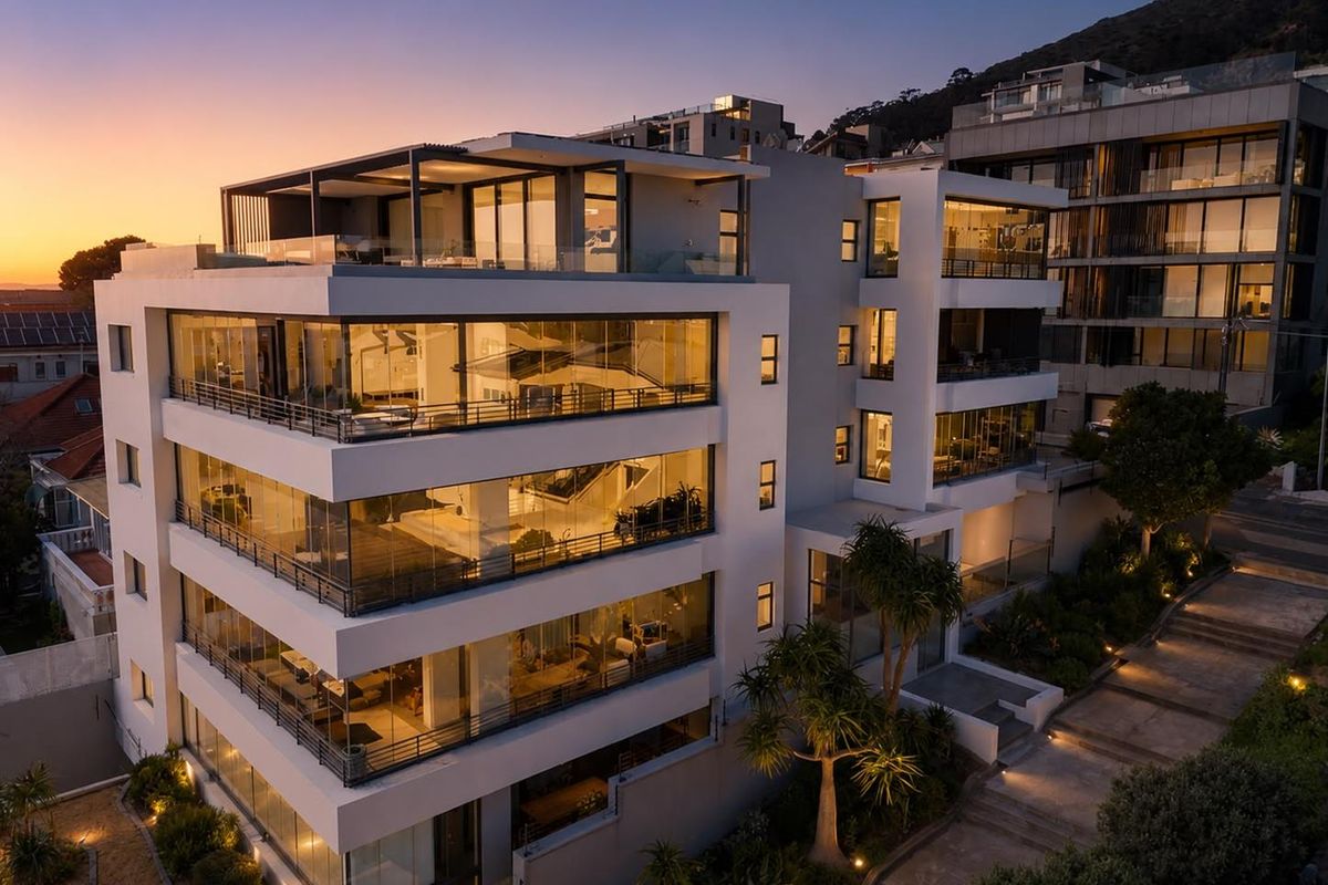 Aerial view of a modern multi-story apartment building at dusk, featuring extensive glass facades, private balconies, and integrated exterior lighting.