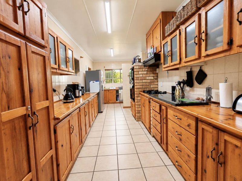 A galley-style kitchen featuring extensive timber cabinetry, a brick feature wall, built-in oven, gas cooktop, and tiled flooring.