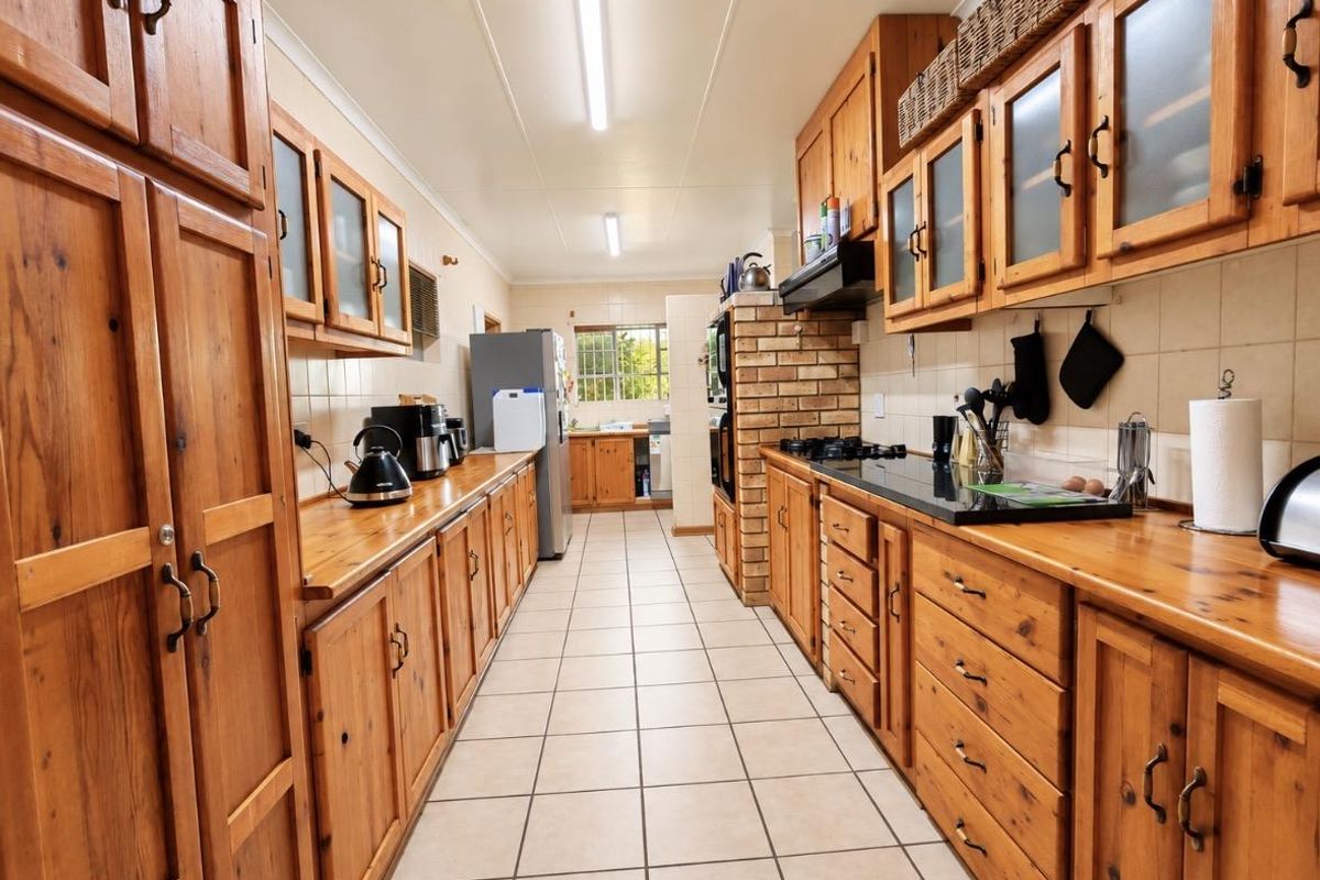 A galley-style kitchen featuring extensive timber cabinetry, a brick feature wall, built-in oven, gas cooktop, and tiled flooring.