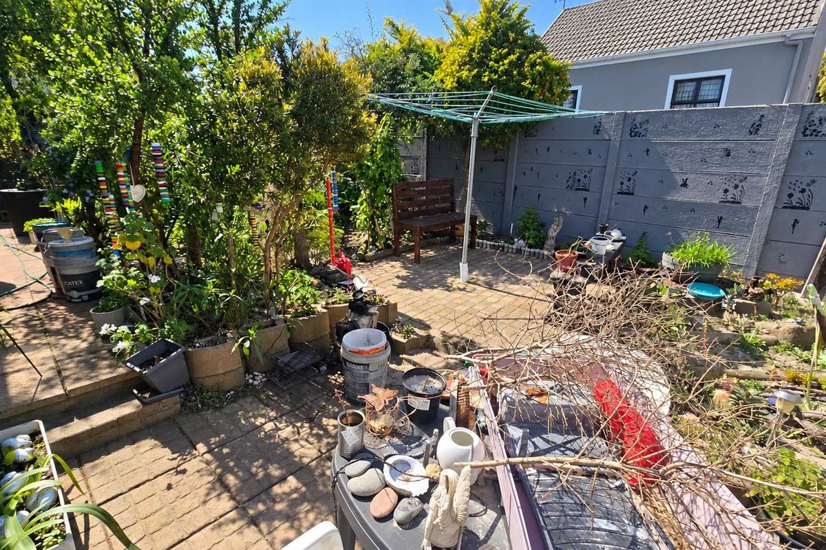A rear garden area featuring paved patio space, established garden beds with retaining walls, and a precast concrete boundary wall.