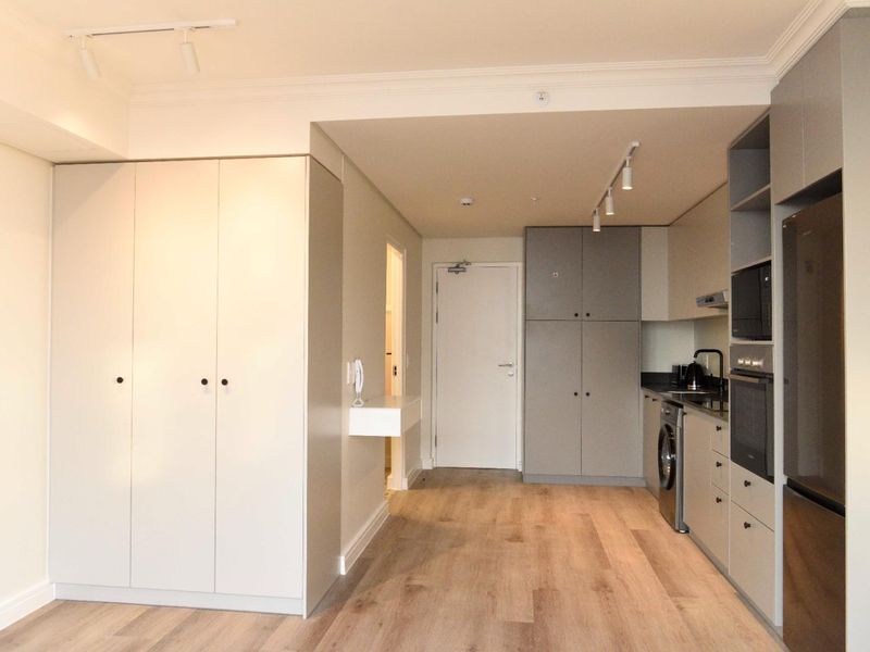 Modern open-plan apartment interior featuring light wood-look flooring, sleek built-in cabinetry, integrated kitchen appliances, and clean neutral finishes throughout.