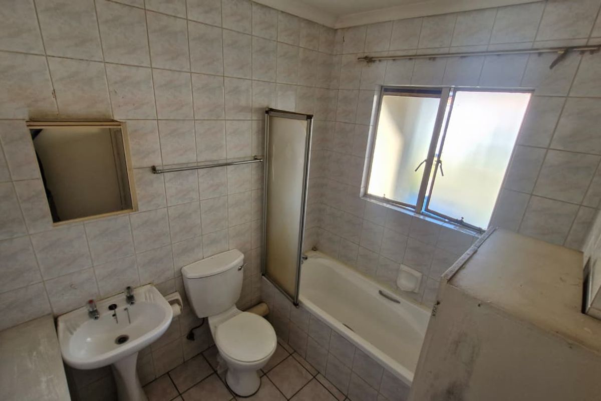 A dated bathroom featuring a pedestal basin, toilet, and bathtub with a shower screen, finished with full-height wall tiling.