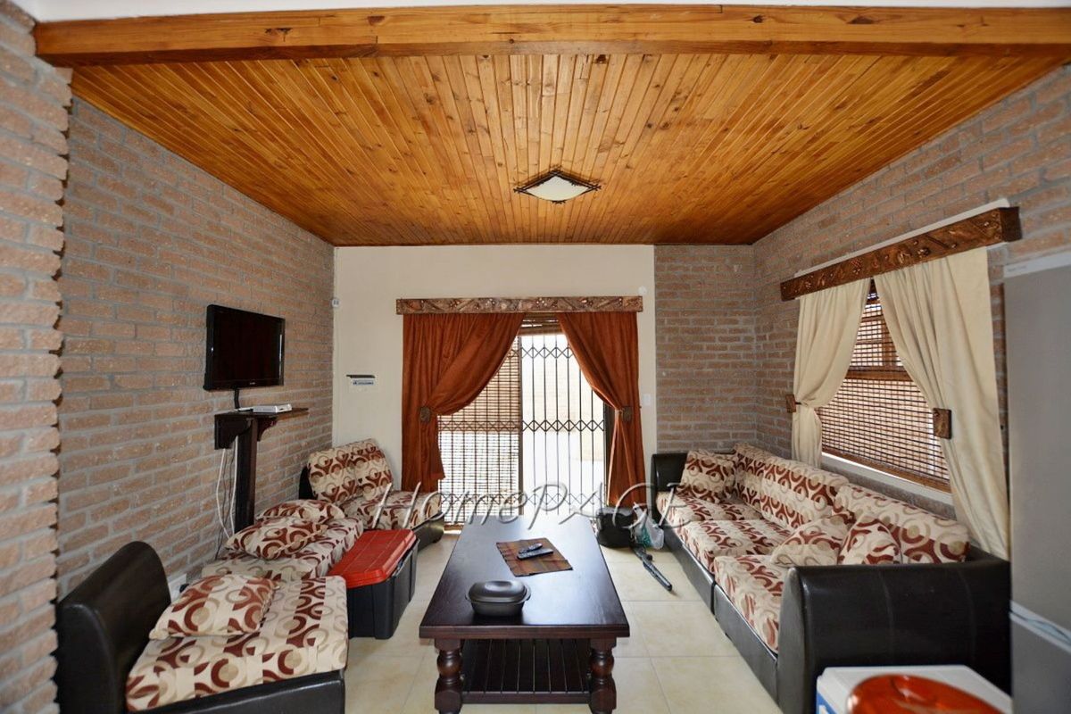 A living room featuring exposed brick walls, a timber-clad ceiling, and tiled flooring, with access to an outdoor area through a security gate.