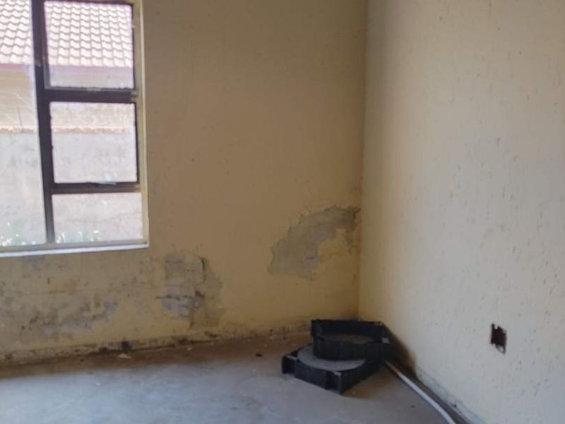 An unfinished bedroom interior featuring exposed ceiling rafters, bare concrete flooring, and visible wall plaster damage requiring renovation.