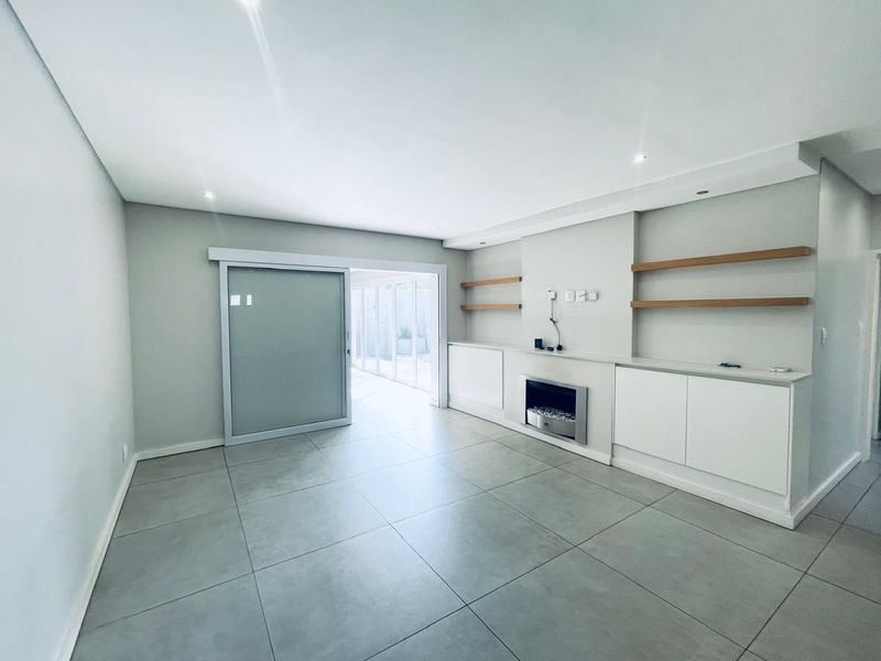 Spacious living area featuring large format floor tiles, built-in cabinetry with floating shelves, a modern recessed fireplace, and sliding glass doors leading outdoors.