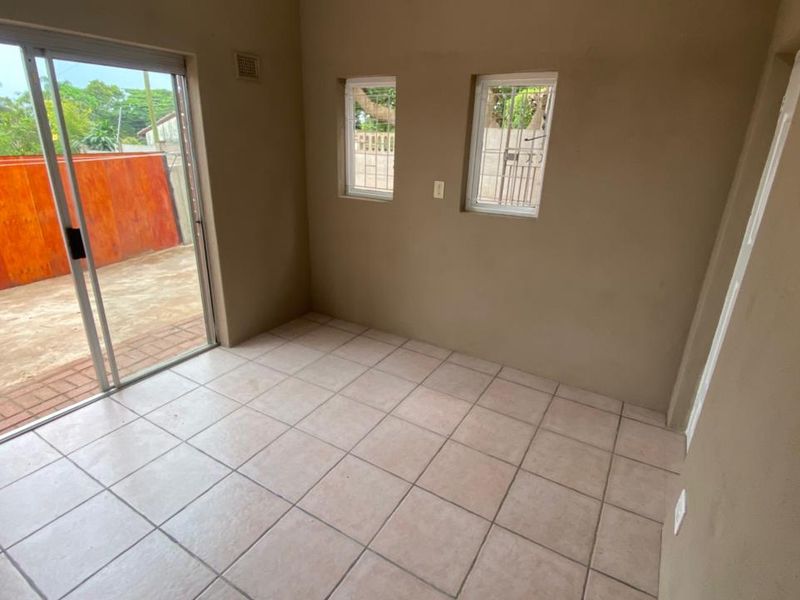 An empty living room featuring ceramic floor tiles, sliding glass doors leading to the exterior, and two casement windows.