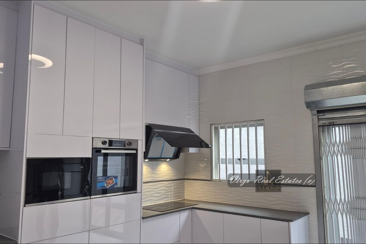 Modern kitchen featuring high-gloss white cabinetry, integrated appliances, sleek hob, extractor fan, and textured wall tiling.