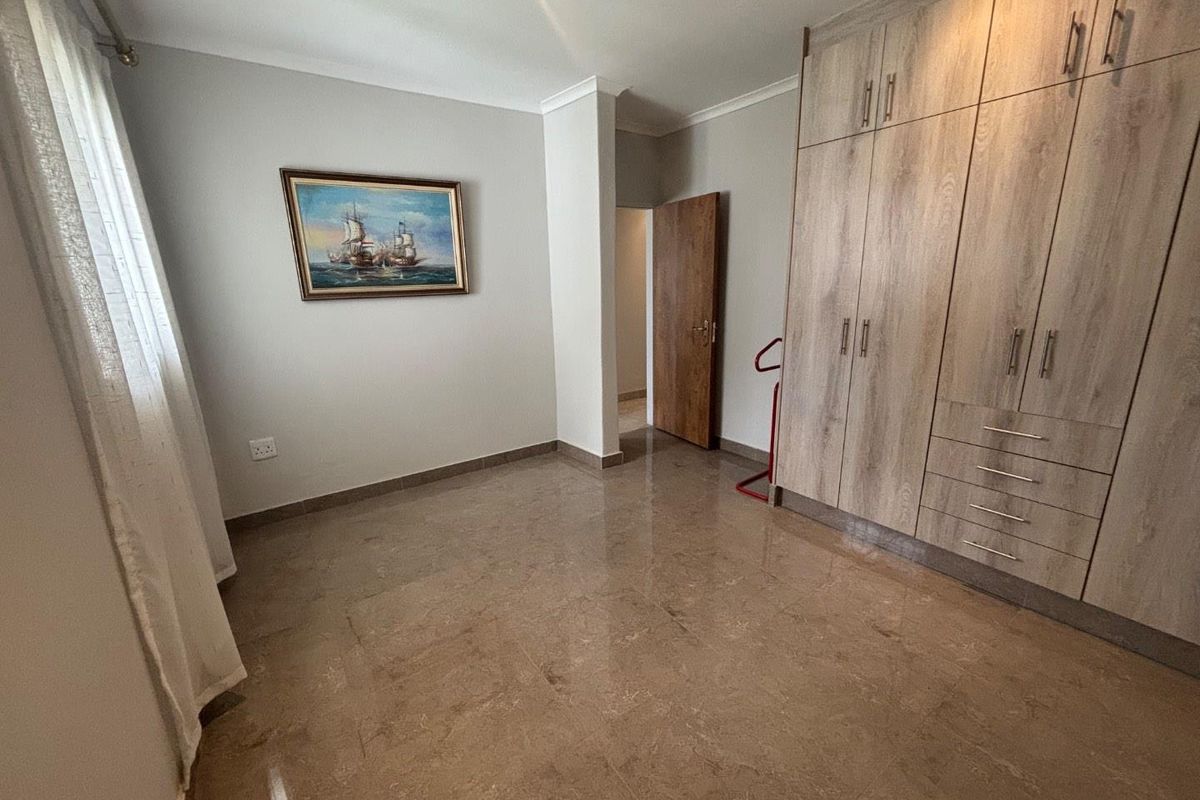 A well-maintained bedroom featuring polished tile flooring, neutral wall finishes, and extensive built-in wooden cabinetry for storage.