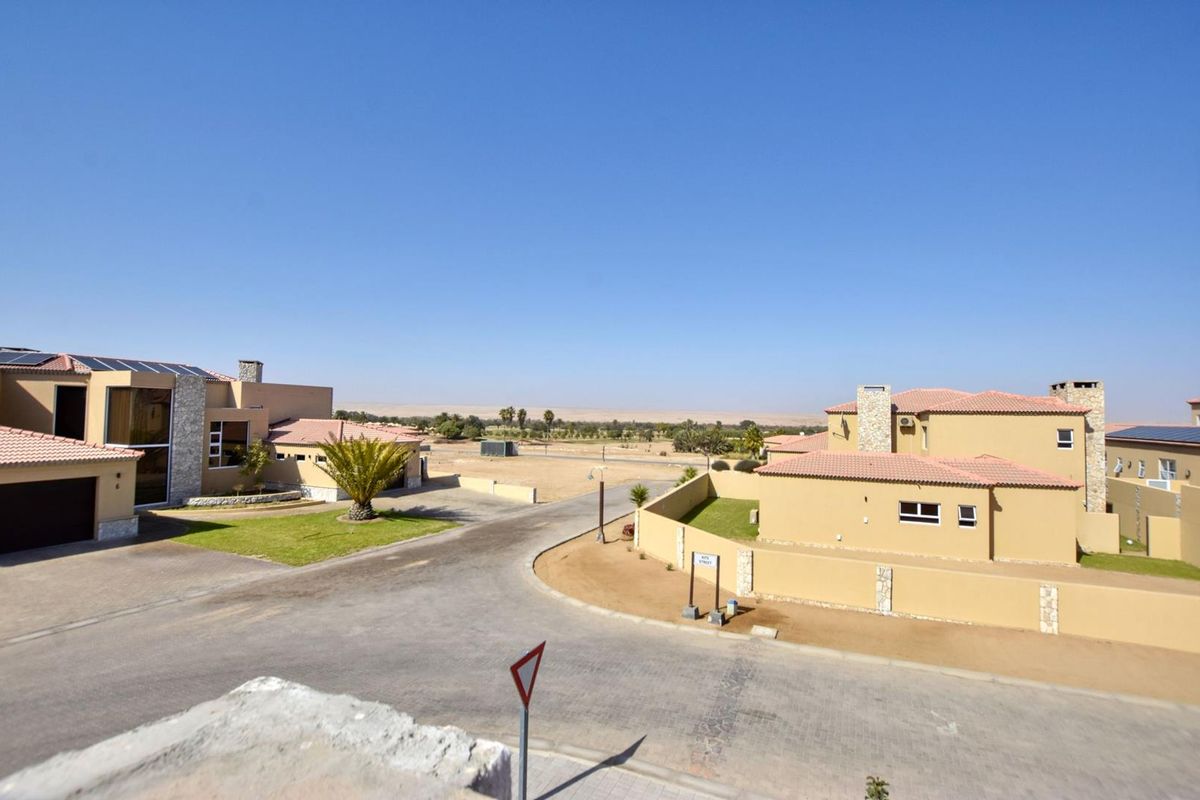 An elevated view of a residential estate street featuring modern houses with tiled roofs, paved driveways, and landscaped garden areas.
