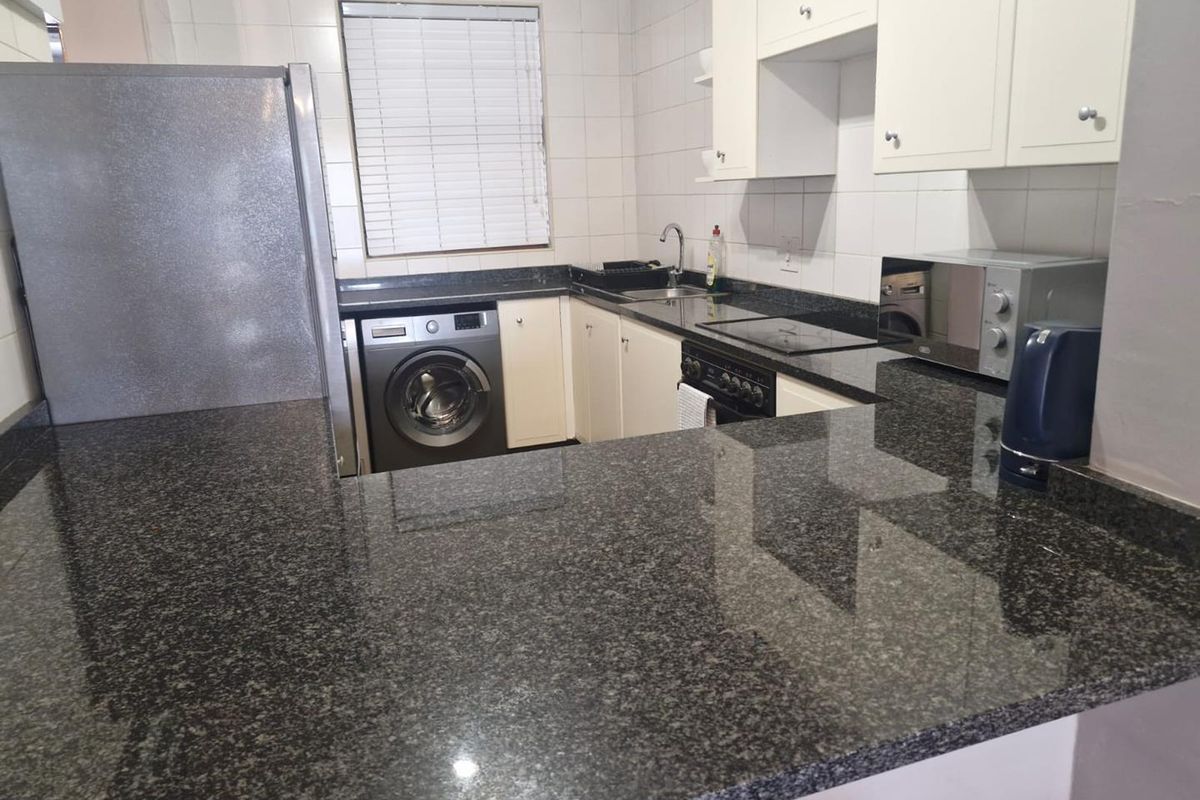 Compact kitchen featuring dark granite countertops, white cabinetry, tiled splashbacks, and integrated laundry appliance space.