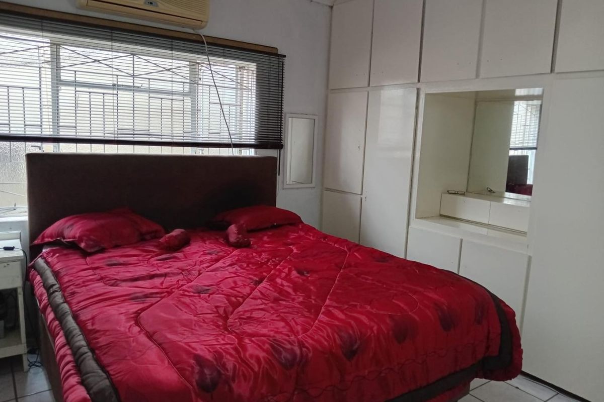 A bedroom featuring built-in cupboards with integrated vanity mirror, tiled flooring, and a wall-mounted air conditioning unit.