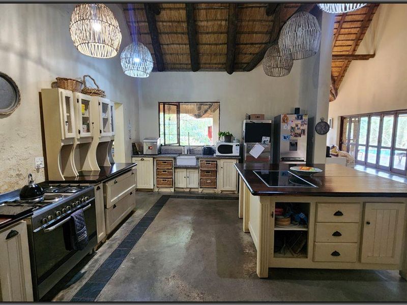 Spacious farmhouse-style kitchen featuring a large central island, timber countertops, gas stove, farmhouse sink, and high vaulted ceilings with exposed thatch and timber beams.