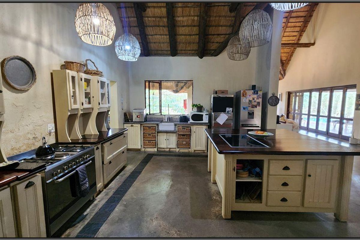 Spacious farmhouse-style kitchen featuring a large central island, timber countertops, gas stove, farmhouse sink, and high vaulted ceilings with exposed thatch and timber beams.