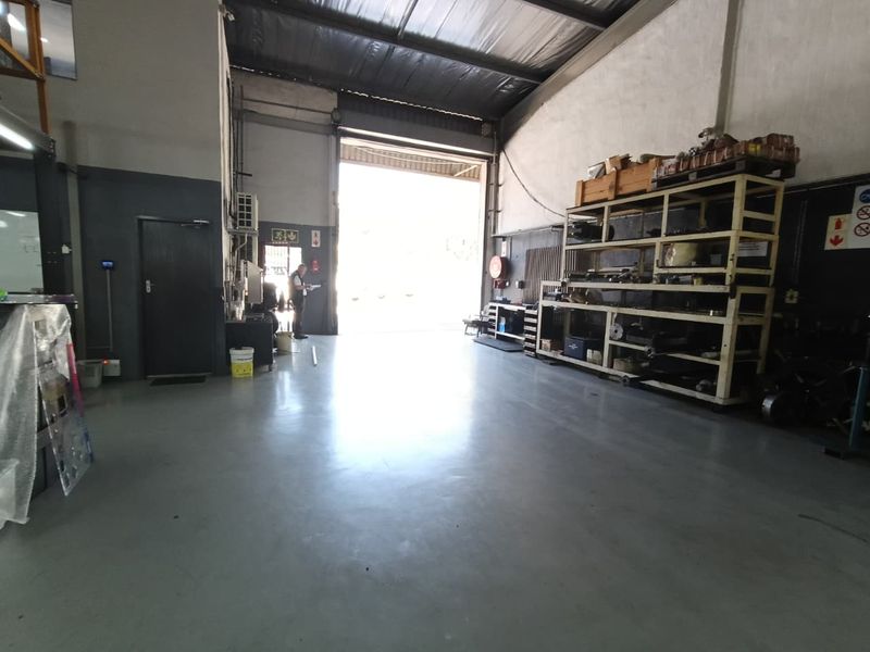 Spacious industrial warehouse unit featuring high ceilings with exposed steel trusses, durable epoxy-coated concrete flooring, and a large roller shutter door for vehicle access.