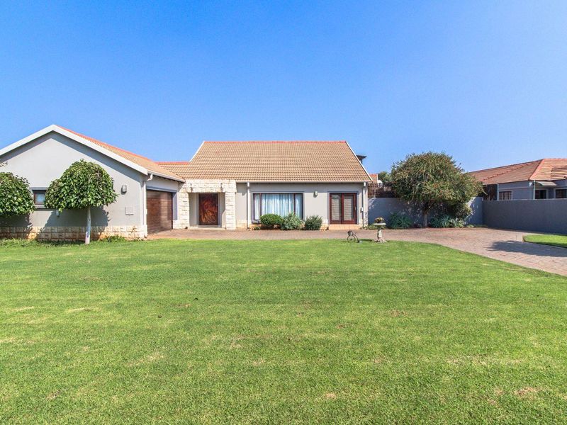 A well-maintained single-story house featuring a tiled roof, stone facade accents, a paved driveway, and a spacious front lawn.