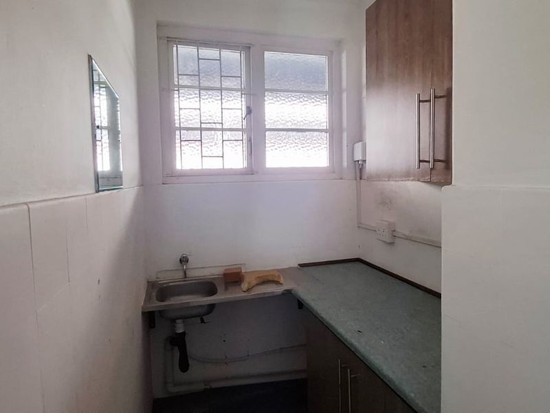 A compact scullery or utility area featuring a stainless steel sink, laminate countertop, and built-in cabinetry, requiring cosmetic updates.