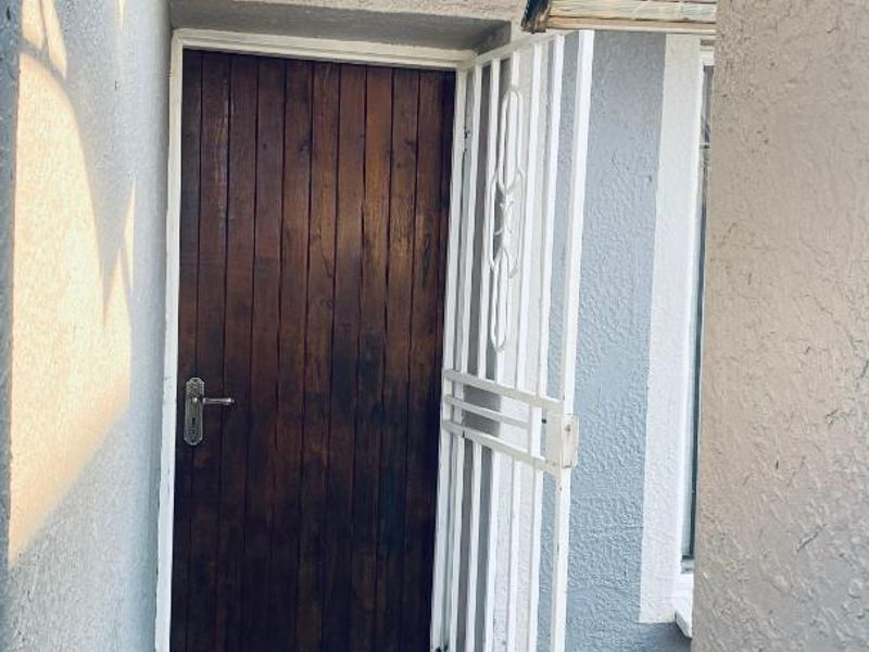 A side entrance featuring a wooden door protected by a white metal security gate and a small overhead awning.