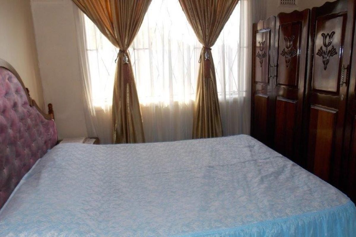 A bedroom featuring a built-in wooden wardrobe and a window with security bars, offering a functional and traditional living space.