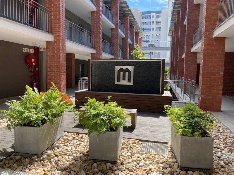 A well-maintained central courtyard area featuring a modern water feature, timber decking, and exposed brick architectural elements within an apartment complex.