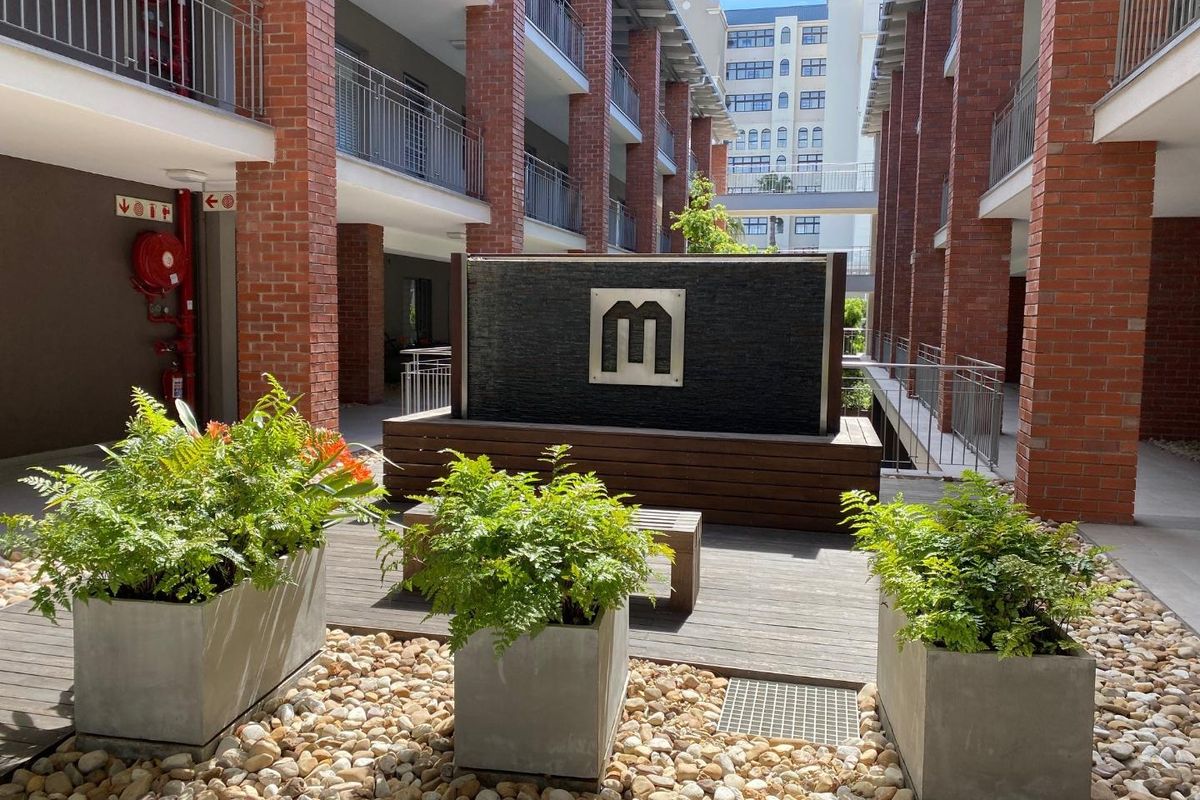 A well-maintained central courtyard area featuring a modern water feature, timber decking, and exposed brick architectural elements within an apartment complex.