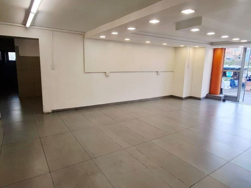 A spacious, vacant commercial office or retail space featuring large glass windows, tiled flooring, and a mix of recessed and strip lighting.